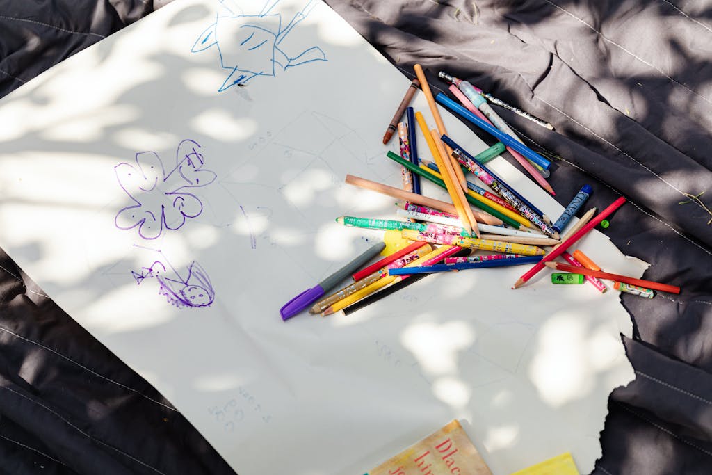 A collection of colored pencils and drawings on white paper under dappled sunlight, fostering creativity.