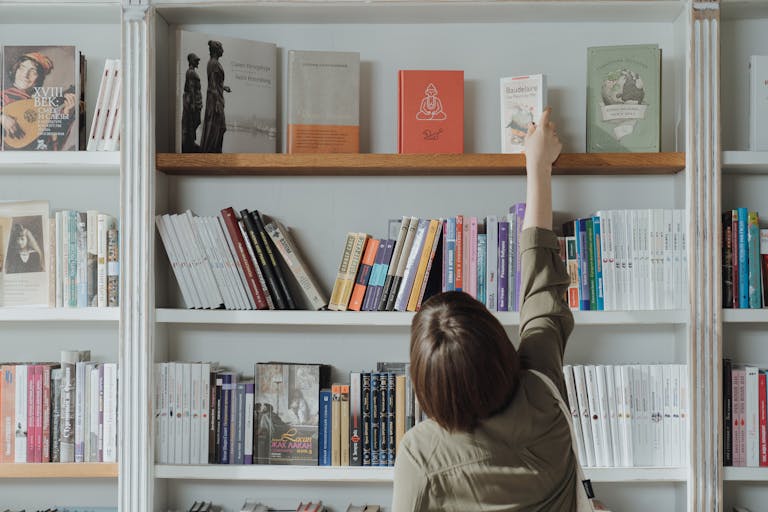 An individual browsing a bookshelf and reaching for a book in a bookstore setting.